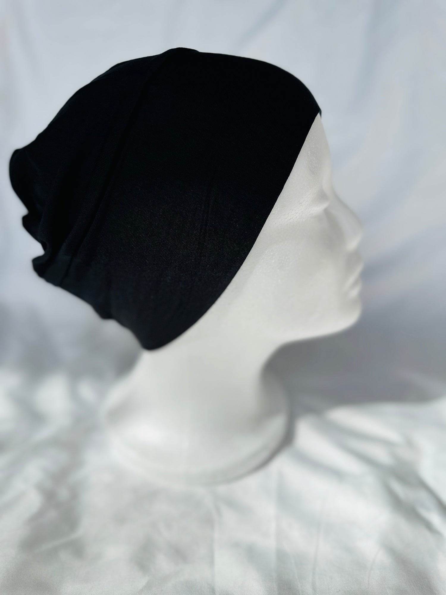 Thin microfiber undercap - barely-there feel under lightweight scarves A soft, stretchable black hijab undercap laid flat on a neutral background, showcasing its smooth texture and clean stitching.