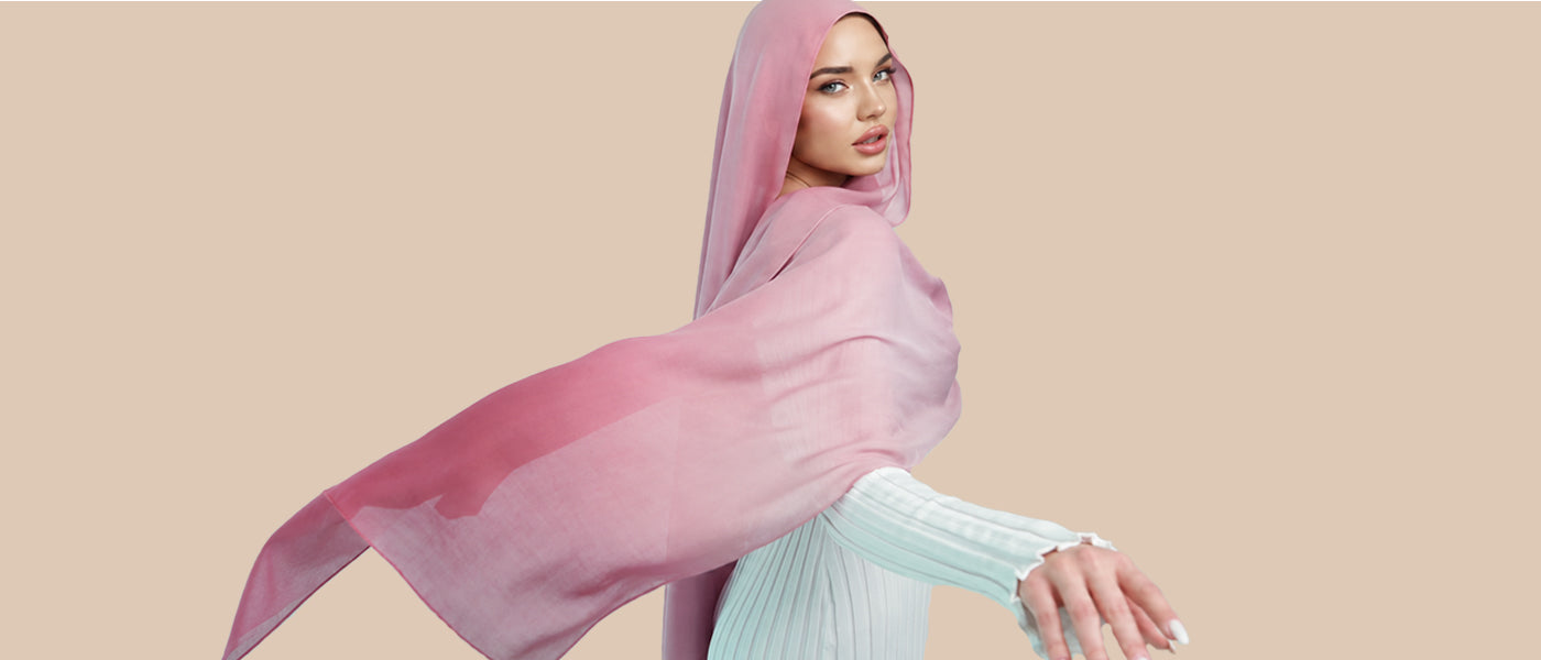 Woman wearing a blush pink chiffon hijab styled in a flowing side drape against a neutral beige background